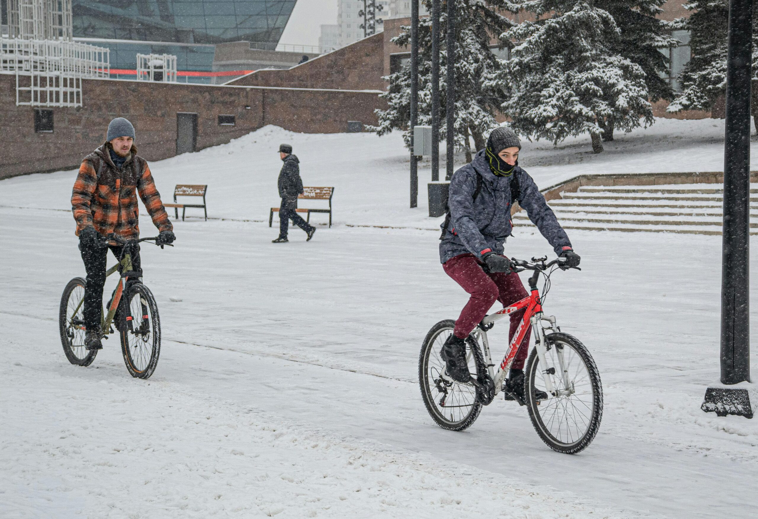 Two cyclists ride through a snow-covered park, showcasing winter activities and urban lifestyle.